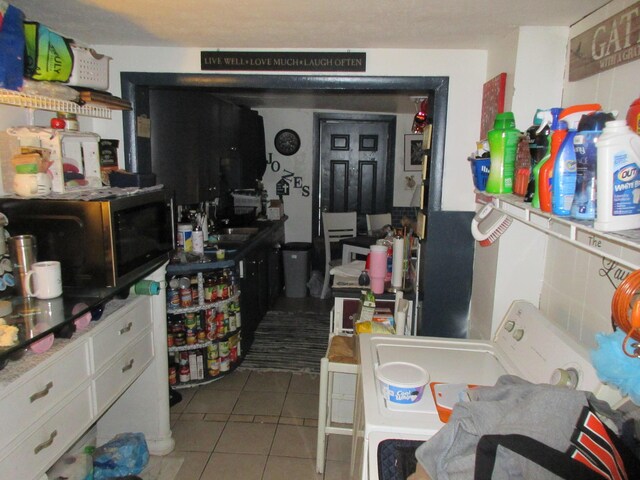 kitchen featuring stainless steel microwave, tile patterned floors, washer / dryer, a sink, and white cabinetry