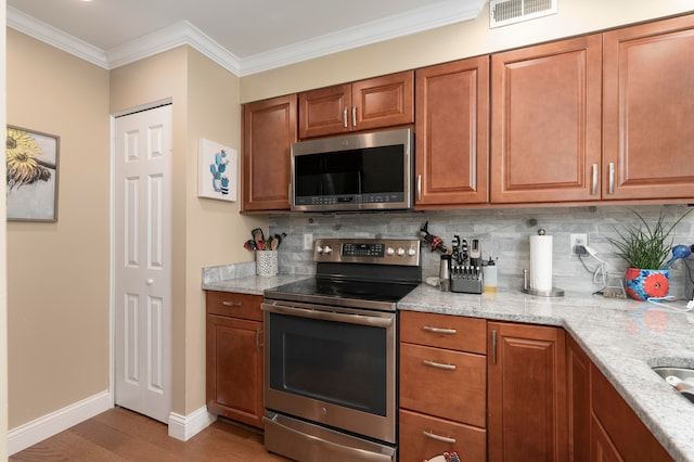 kitchen with appliances with stainless steel finishes, light hardwood / wood-style floors, backsplash, light stone countertops, and crown molding