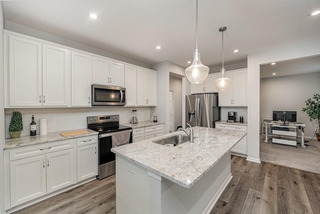 kitchen with hanging light fixtures, white cabinets, stainless steel appliances, a kitchen island with sink, and hardwood / wood-style floors