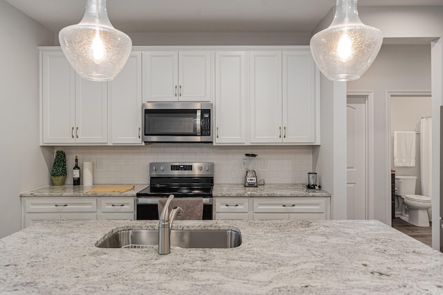 kitchen featuring sink, white cabinets, stainless steel appliances, decorative light fixtures, and light stone countertops