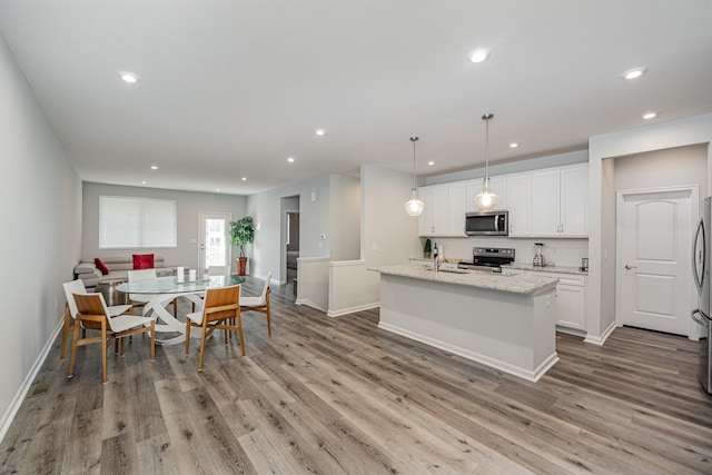 kitchen featuring appliances with stainless steel finishes, light hardwood / wood-style floors, pendant lighting, and an island with sink