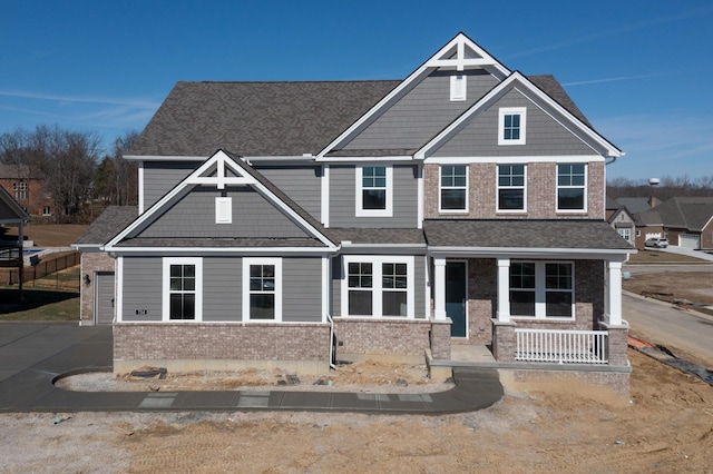 craftsman house featuring driveway, a porch, a shingled roof, and brick siding