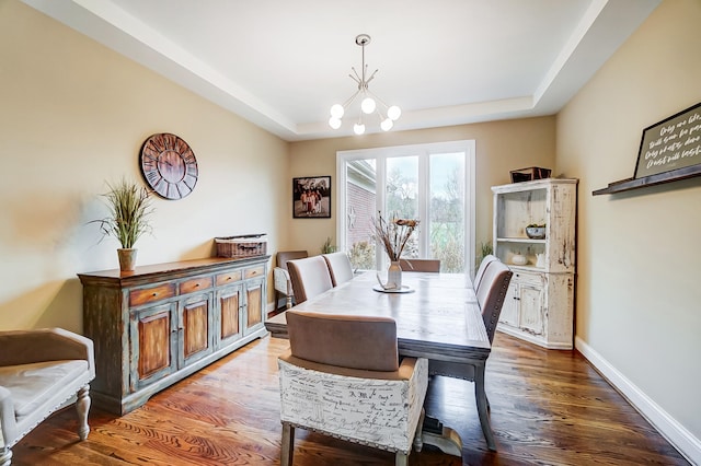 dining space with dark hardwood / wood-style flooring, a tray ceiling, and a chandelier