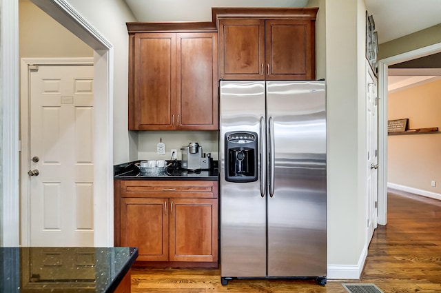 kitchen featuring wood-type flooring, stainless steel fridge with ice dispenser, and dark stone countertops