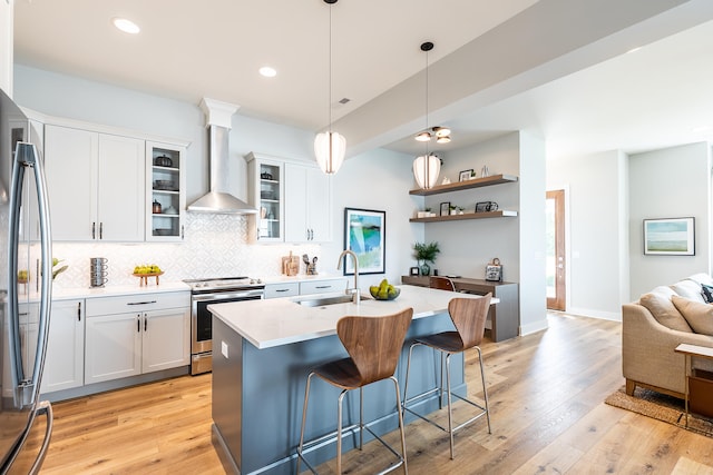 kitchen with white cabinets, appliances with stainless steel finishes, wall chimney exhaust hood, and light hardwood / wood-style flooring