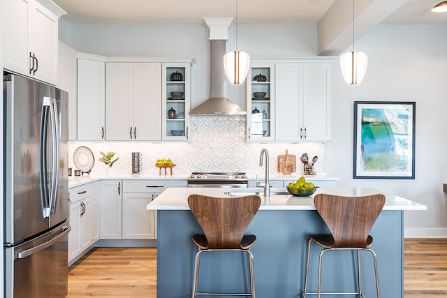 kitchen featuring wall chimney exhaust hood, a kitchen island with sink, stainless steel appliances, and white cabinetry