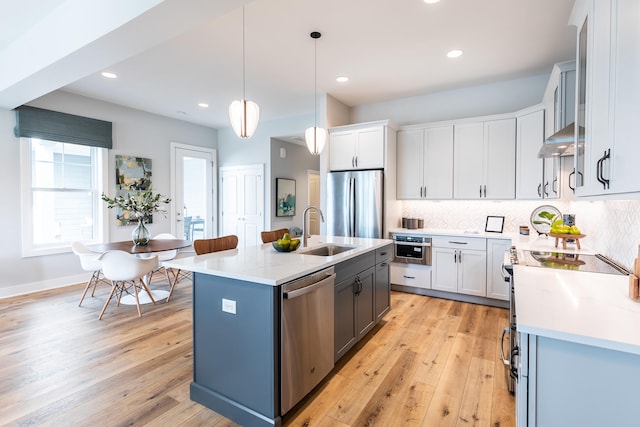 kitchen with hanging light fixtures, stainless steel appliances, light hardwood / wood-style flooring, a center island with sink, and sink