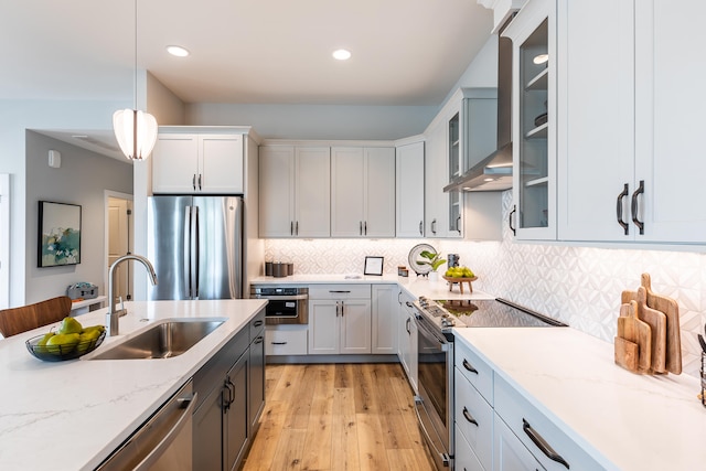 kitchen with light hardwood / wood-style floors, sink, hanging light fixtures, wall chimney range hood, and stainless steel appliances