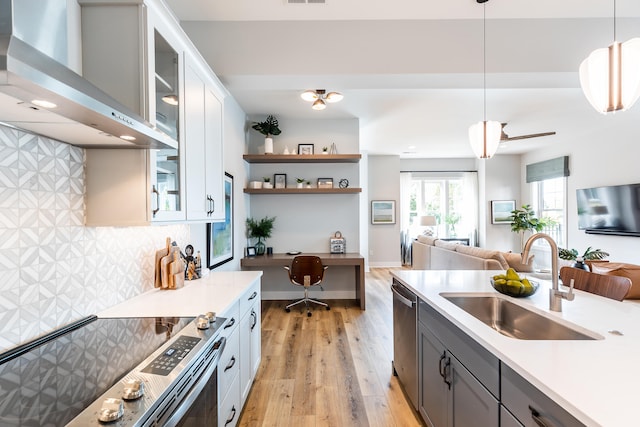 kitchen with built in desk, hanging light fixtures, white cabinets, wall chimney exhaust hood, and sink