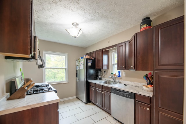 kitchen featuring sink, a textured ceiling, stainless steel appliances, dark brown cabinetry, and light tile patterned floors