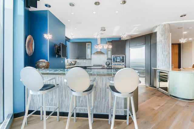 kitchen featuring decorative backsplash, stainless steel microwave, a breakfast bar, light hardwood / wood-style floors, and wall chimney exhaust hood