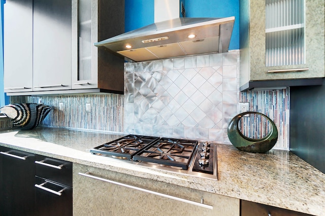 kitchen featuring light stone counters, ventilation hood, stainless steel gas stovetop, and tasteful backsplash