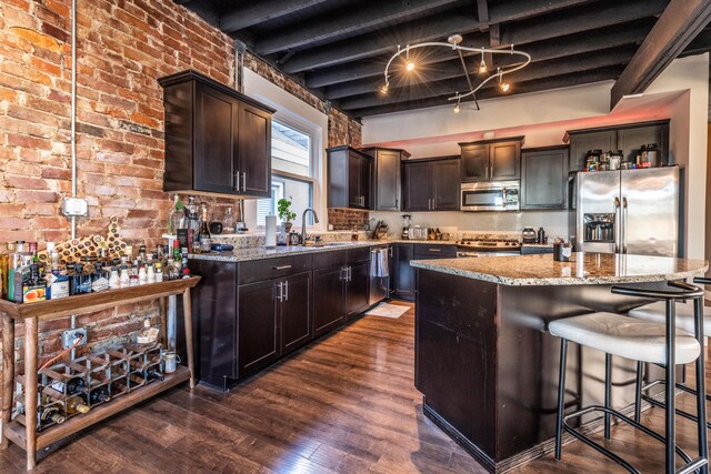 kitchen featuring light stone counters, a breakfast bar area, beamed ceiling, appliances with stainless steel finishes, and a kitchen island