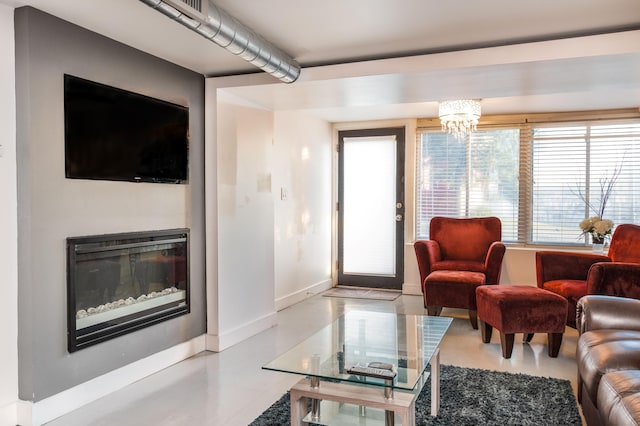 living area with baseboards, an inviting chandelier, and a glass covered fireplace
