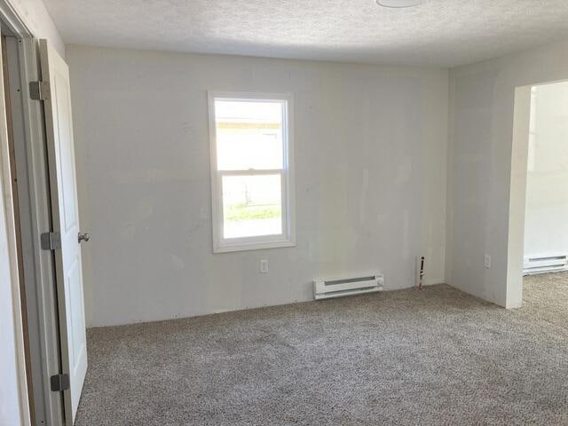 carpeted spare room with a baseboard radiator and a textured ceiling