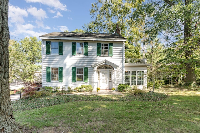 colonial house with a balcony, a chimney, and a front yard