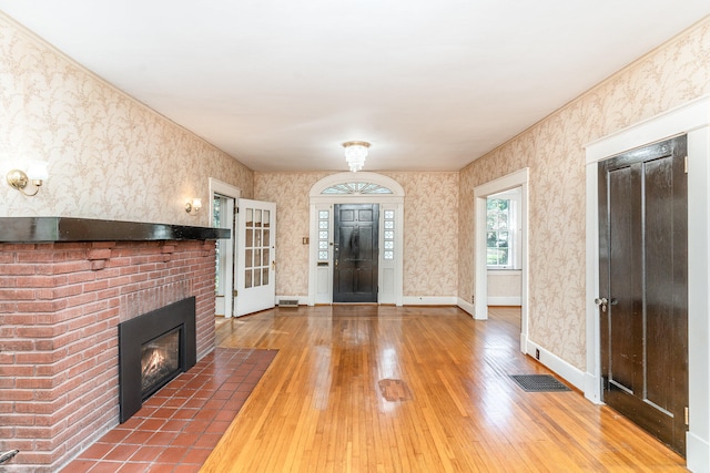 foyer entrance with wallpapered walls, visible vents, baseboards, and wood finished floors