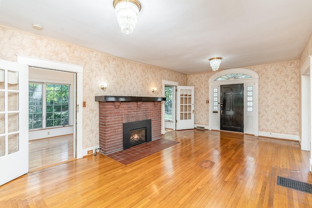 unfurnished living room featuring wallpapered walls, a brick fireplace, visible vents, and wood finished floors