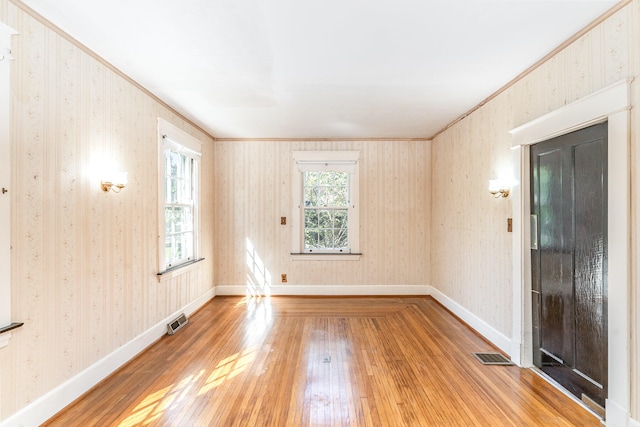 empty room with light wood-style floors, visible vents, and wallpapered walls