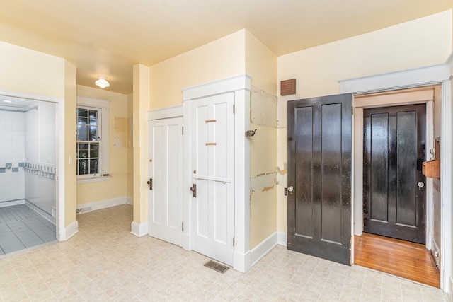 foyer entrance with light floors, baseboards, and visible vents