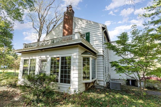 view of property exterior featuring a balcony, a chimney, and cooling unit