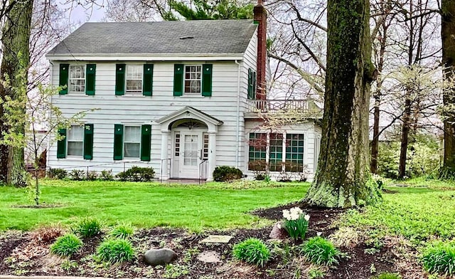 colonial-style house with a shingled roof, a front yard, and a chimney