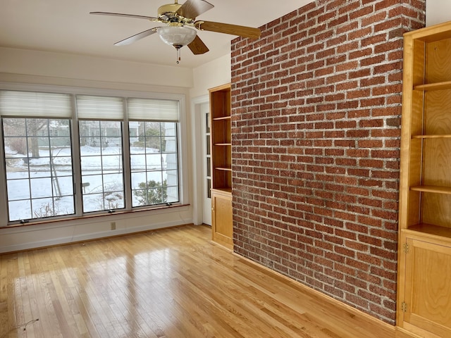 unfurnished room featuring a ceiling fan, light wood-type flooring, and brick wall