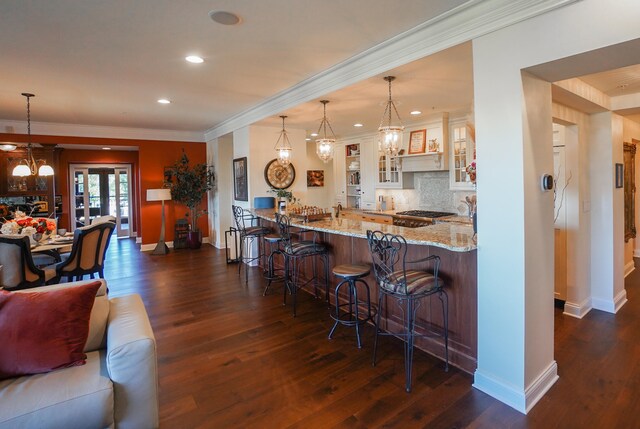 kitchen with light stone counters, hanging light fixtures, tasteful backsplash, dark hardwood / wood-style floors, and a kitchen bar