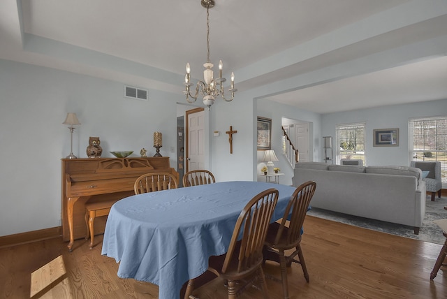 dining room with a tray ceiling, visible vents, wood finished floors, and stairway