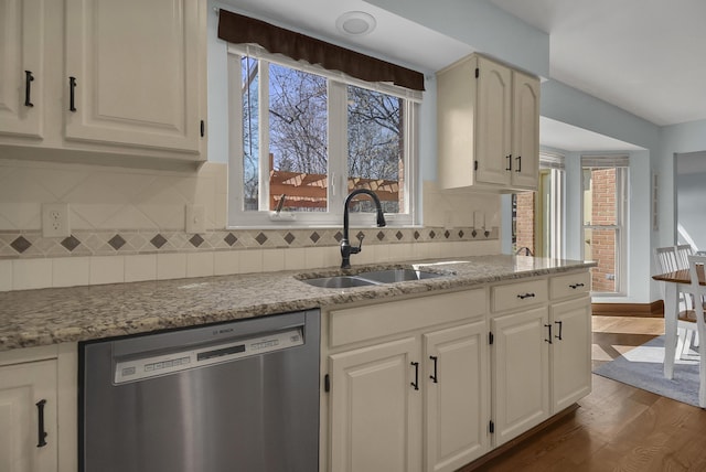 kitchen with tasteful backsplash, dishwasher, light stone counters, dark wood-style floors, and a sink