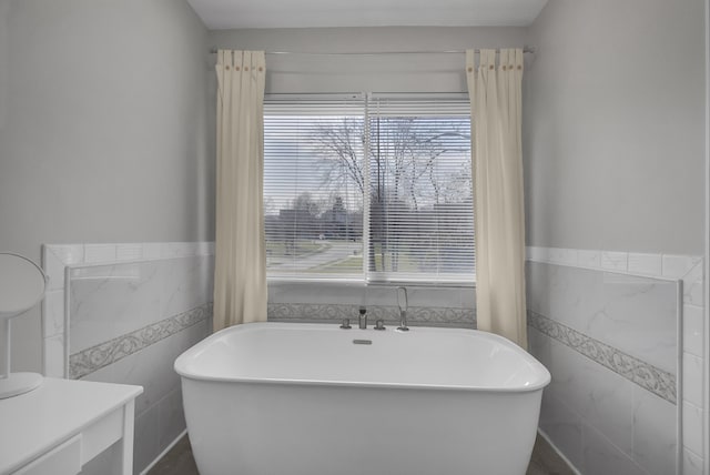 bathroom featuring a wainscoted wall, a freestanding bath, and tile walls