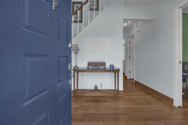 foyer featuring baseboards, wood finished floors, and stairs