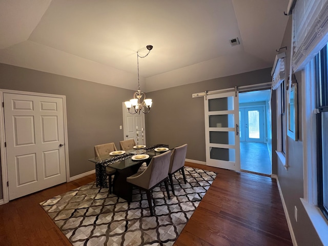 dining space with a raised ceiling, a barn door, a notable chandelier, and dark hardwood / wood-style flooring