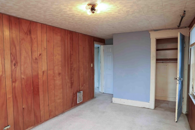 unfurnished bedroom with light colored carpet, a closet, and wood walls