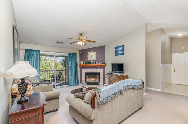 living room featuring a textured ceiling, a tiled fireplace, vaulted ceiling, light colored carpet, and ceiling fan