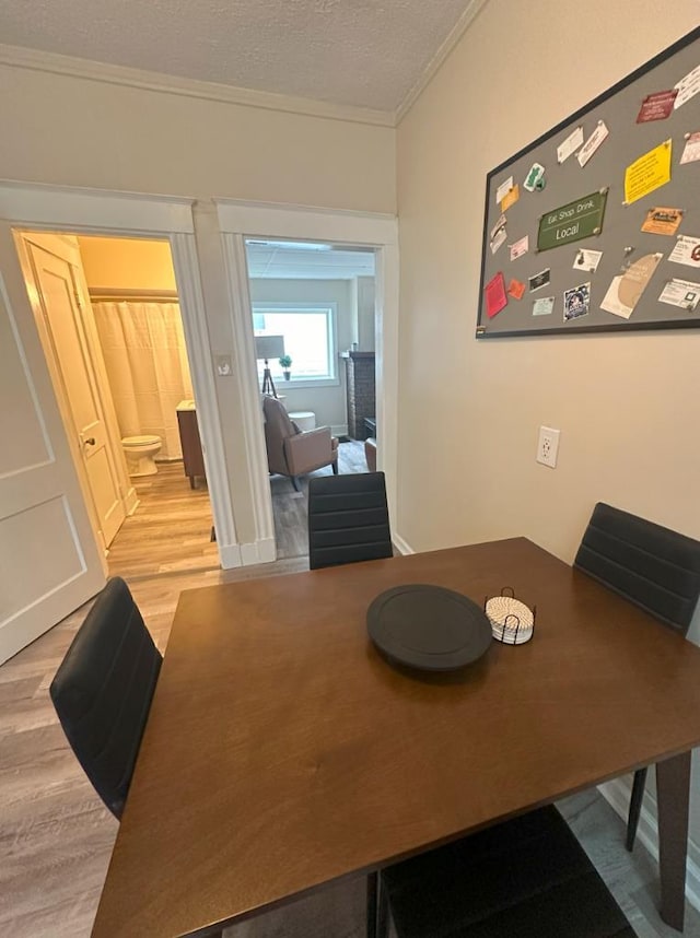 dining space with ornamental molding, light hardwood / wood-style flooring, a fireplace, and a textured ceiling