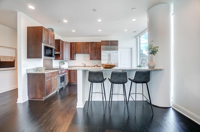 kitchen with built in appliances, light stone countertops, dark wood-type flooring, and a kitchen breakfast bar