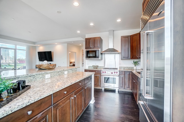 kitchen with light stone countertops, premium appliances, wall chimney exhaust hood, and dark hardwood / wood-style floors