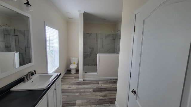 bathroom with hardwood / wood-style floors, toilet, tiled shower, vanity, and crown molding