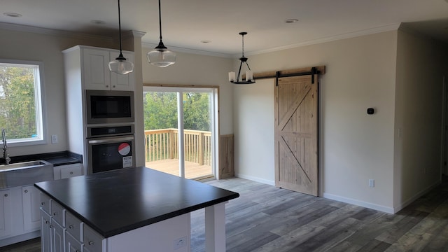 kitchen with a barn door, dark hardwood / wood-style flooring, stainless steel appliances, pendant lighting, and white cabinets