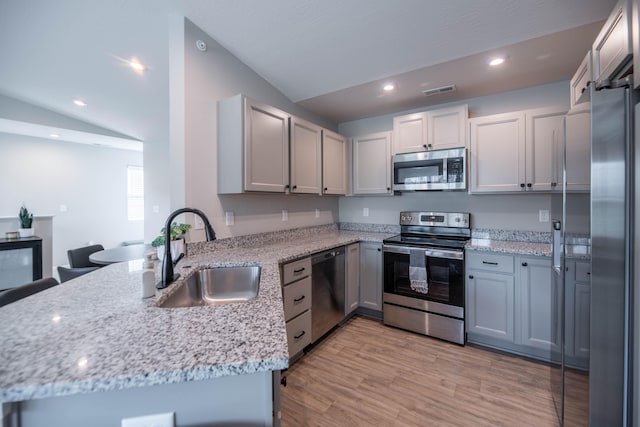 kitchen featuring lofted ceiling, kitchen peninsula, sink, light wood-type flooring, and appliances with stainless steel finishes