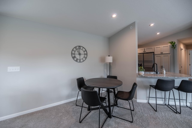 carpeted dining area featuring sink and vaulted ceiling