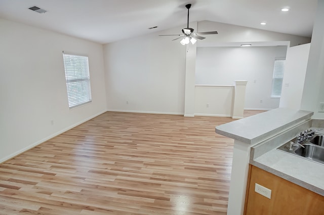 unfurnished living room with ceiling fan, lofted ceiling, sink, and light wood-type flooring