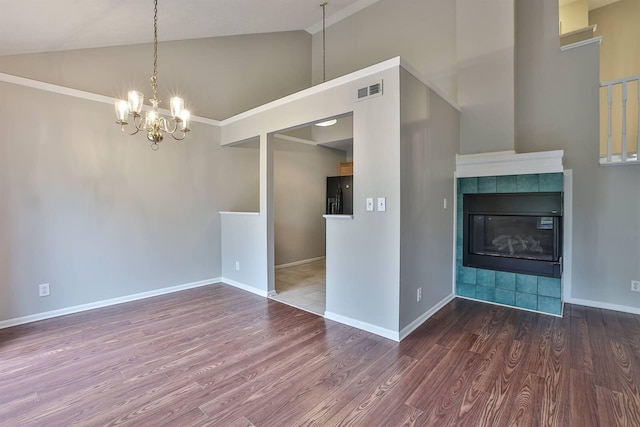 unfurnished living room featuring lofted ceiling, wood-type flooring, a tile fireplace, and an inviting chandelier