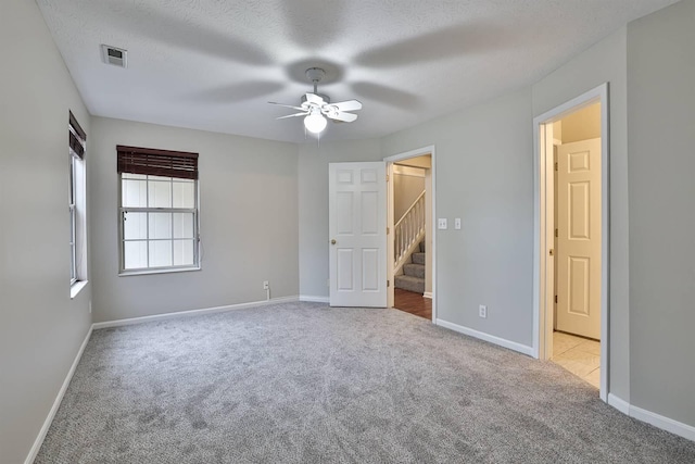 unfurnished bedroom with ceiling fan, light colored carpet, and a textured ceiling