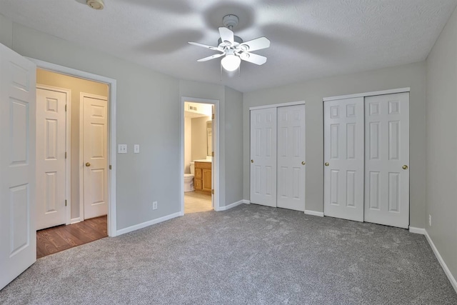 unfurnished bedroom with ensuite bathroom, a textured ceiling, carpet, multiple closets, and ceiling fan