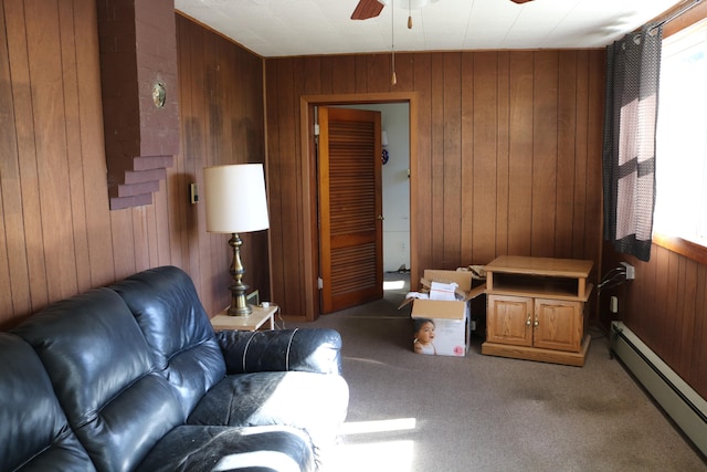 carpeted living room with a baseboard heating unit, wooden walls, and ceiling fan