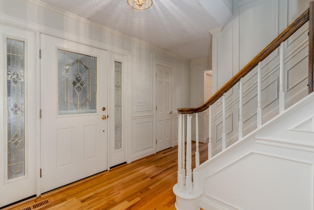 foyer with ornamental molding, light wood-type flooring, and a textured ceiling