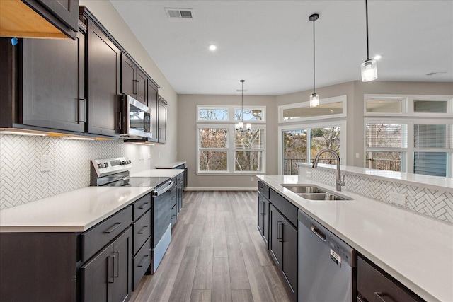 kitchen featuring decorative light fixtures, light countertops, appliances with stainless steel finishes, a sink, and dark brown cabinets