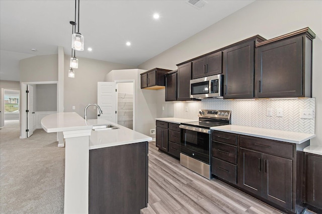 kitchen featuring appliances with stainless steel finishes, hanging light fixtures, a sink, light countertops, and backsplash